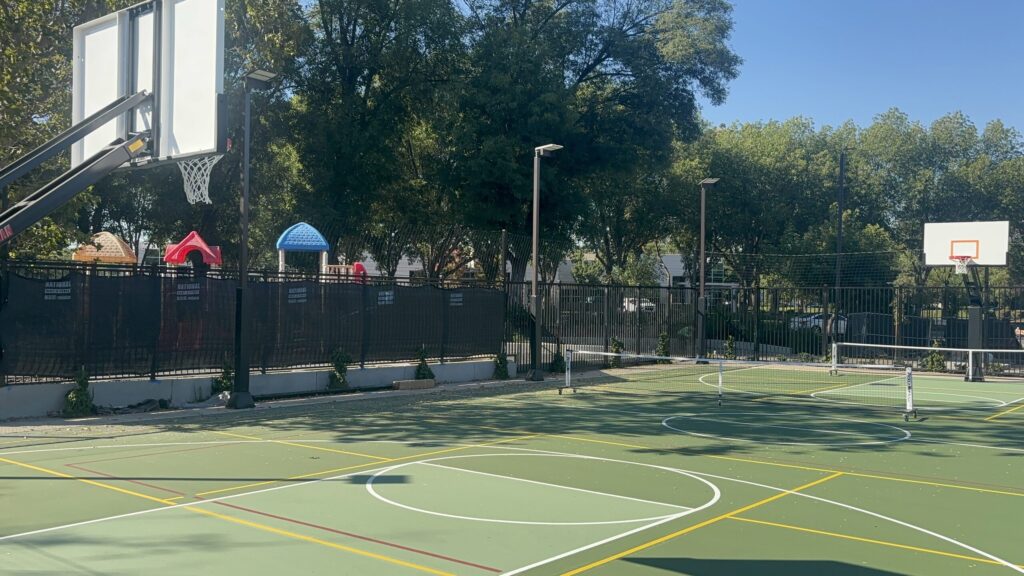 MCC East Bay outdoor court: a basketball hoop in the foreground, a second hoop at the far end, painted basketball and pickleball lines, and portable pickleball nets.